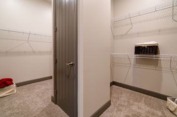 A small closet with a grey door and a wire shelf with a basket on it.